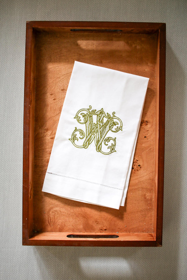 White linen towel with green "W" embroidered on wooden tray