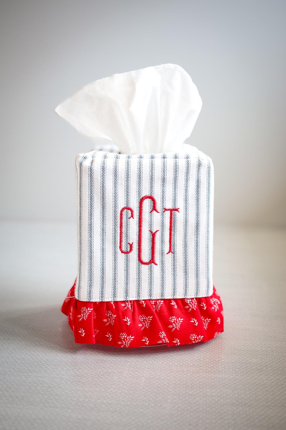 blue ticking stripe tissue box cover with red ruffle detailing and red custom embroidered monogram on white background