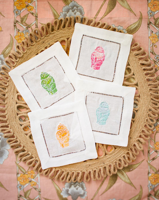 four embroidered ginger jar cocktail napkins on rattan background