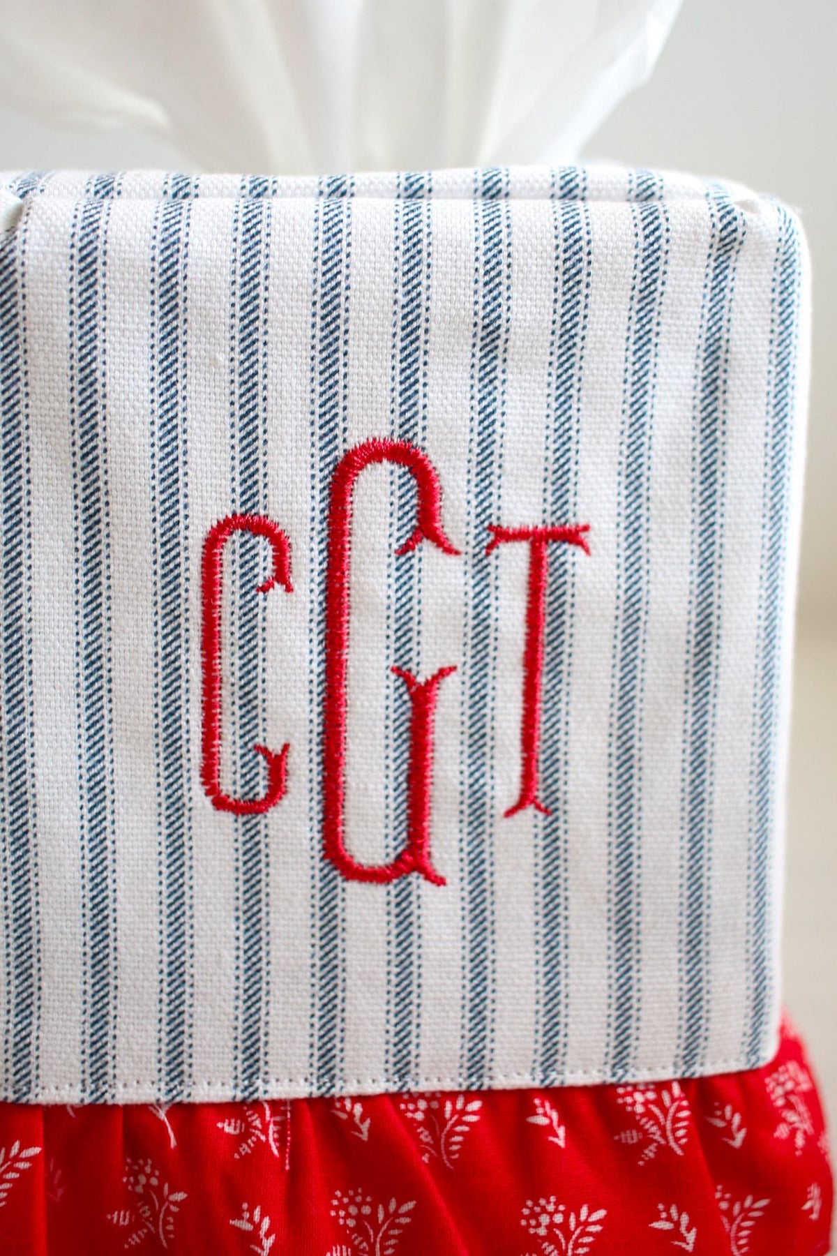 blue ticking stripe tissue box cover with red ruffle detailing and red custom embroidered monogram on white background