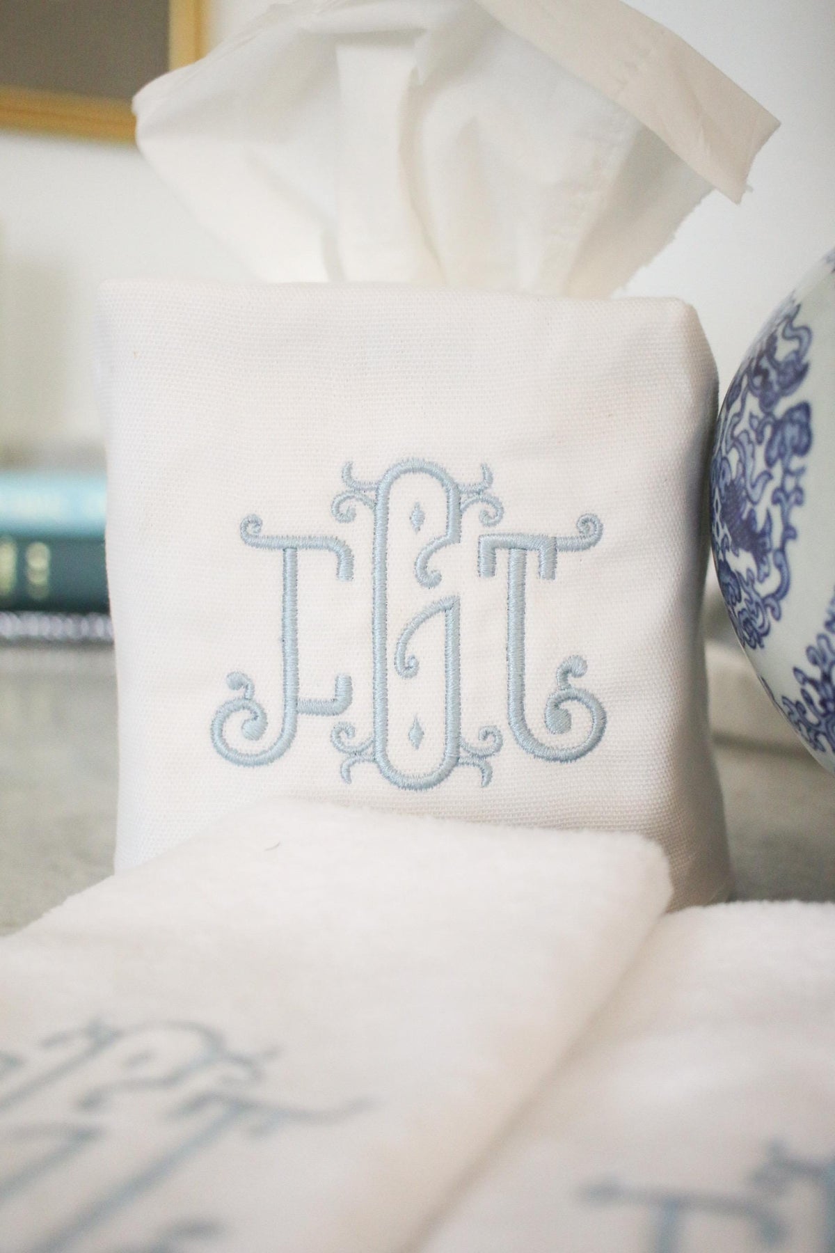 White cotton tissue box cover with embroidered triple-letter monogram in blue thread, matching fingertip towels for bathroom décor.