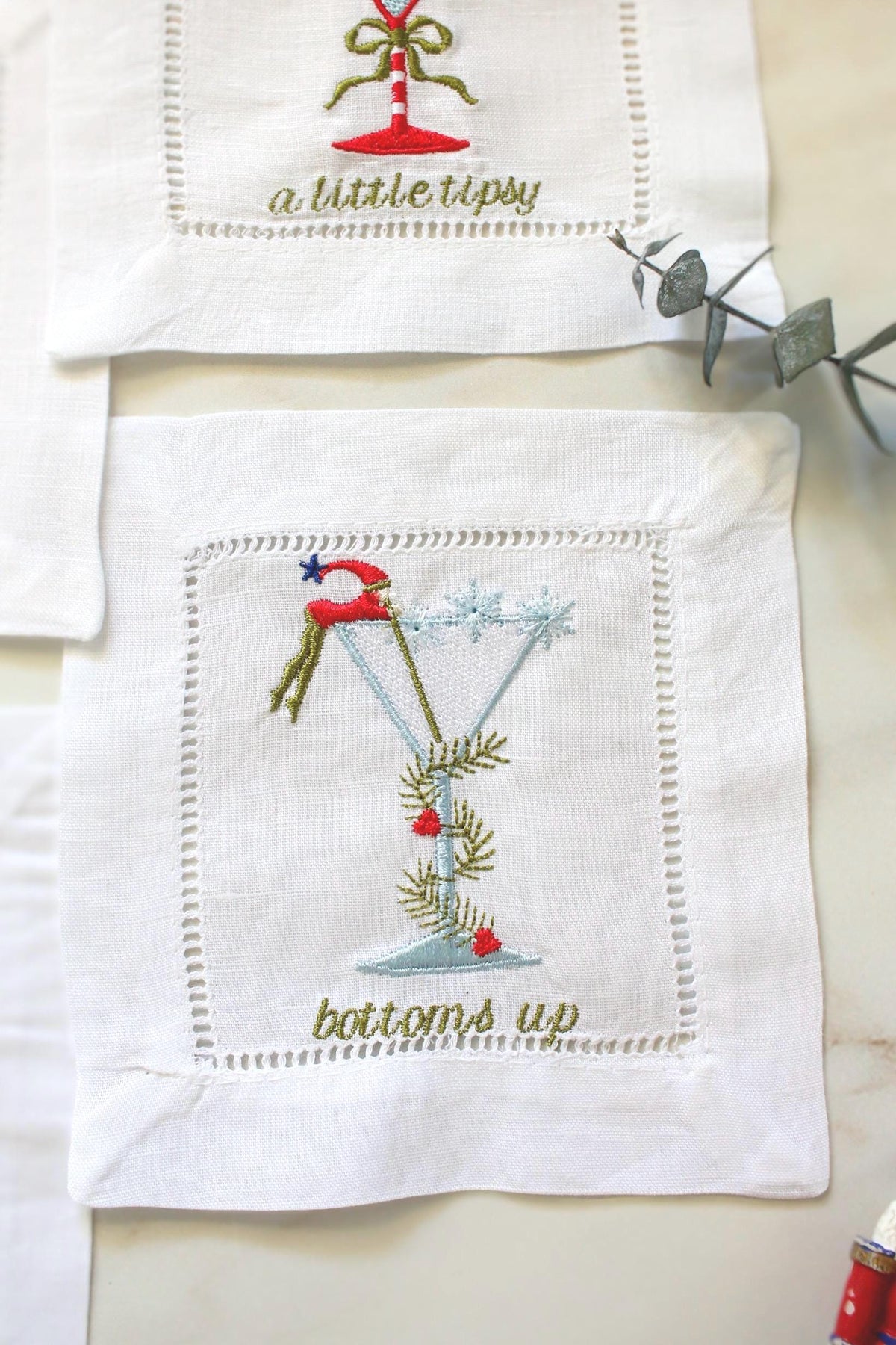 Festive embroidered cocktail napkin – martini glass with Santa hat and pine details, holiday linen hemstitch coaster bottoms up.