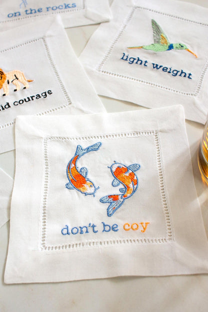 Koi fish embroidered linen cocktail napkin with the phrase Don't Be Coy